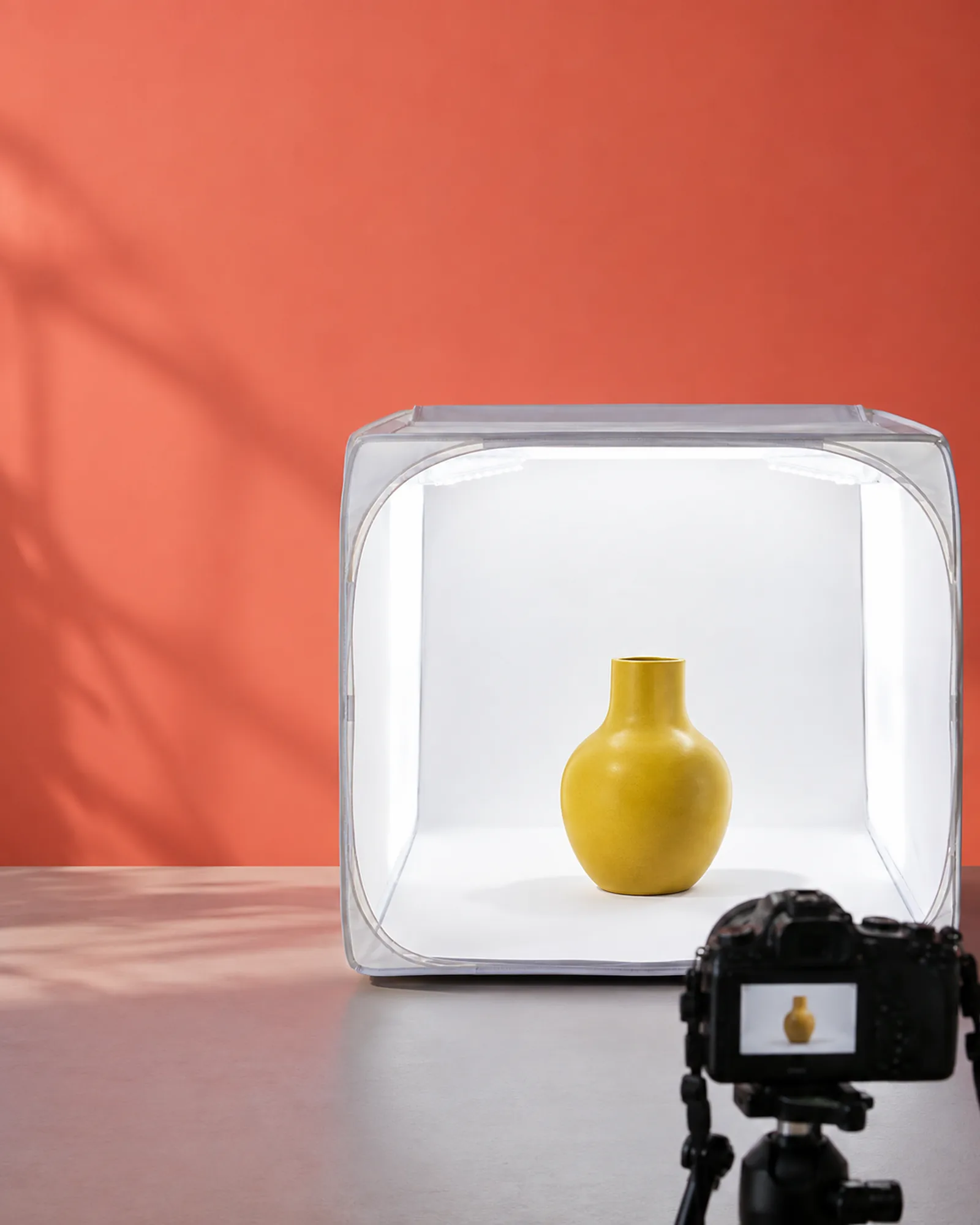 A yellow vase in a glowing light tent against a coral wall